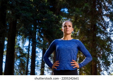 Beautiful Blonde Active Strong Sporty Fit Fitness Model Woman Athlete Standing With Hands On Hips Looking Off Motivational Determined In Green Redwood Forrest Workout Outdoors Exercise