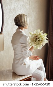 Beautiful Blonde Bride With A Calla Lilies Bouquet In A Bright Hotel Room. Festive Morning, Engagement Party, Happy Couple, Luxurious Celebration, Trende Fashion Bride S Pantsuit.