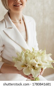 Beautiful Blonde Bride With A Calla Lilies Bouquet In A Bright Hotel Room. Festive Morning, Engagement Party, Happy Couple, Luxurious Celebration, Trendy Fashion Brides Pantsuit.