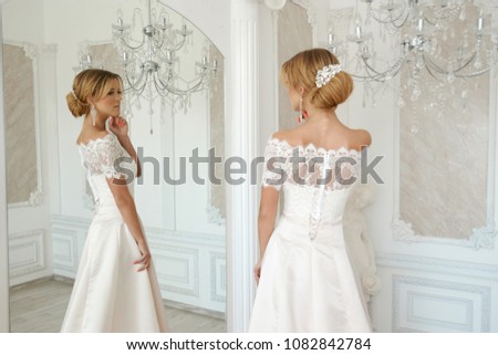 Beautiful blonde bride posing in white elegant dress in bright luxury interior with mirror