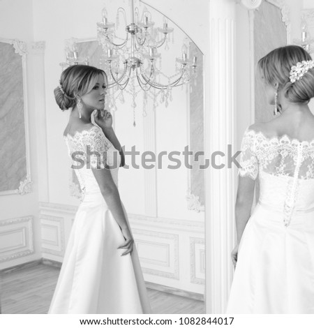 Beautiful blonde bride posing in white elegant dress in bright luxury interior with mirror