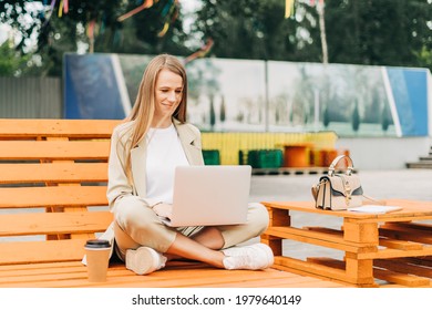 Beautiful Blonde Business Woman Working At Laptop Sit Down On Bench Outside On A Urban City Street. Happy Lady Girl In Suit Distance Learning, Education And Online Shopping.