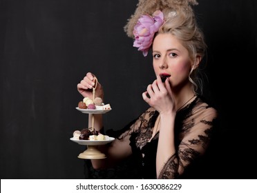 Beautiful blonde countess with chocolate candies on dark background - Shutterstock ID 1630086229