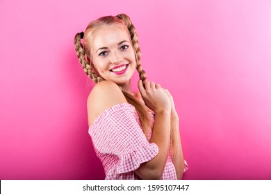 beautiful blonde czech photo model with pigtails in a white pink checked blouse isolated standing against pink backdrop in studio. happy facial expression. somekind of shyness. free copy space around.