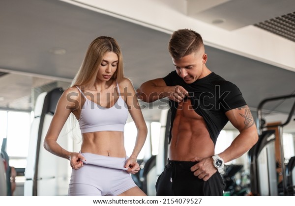 Beautiful blonde\
fitness woman and a handsome man athlete with a muscular body are\
showing off their abdominal abs in the gym. Young healthy athletic\
couple working out\
together