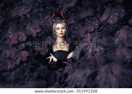 Beautiful blonde girl in a black dress with a pink medieval horns, devilish image, chestnut tree