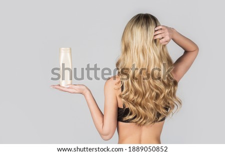 Beautiful blonde girl with a bottle of shampoos in hands. Girl with shiny and long hair. Woman long hair. Woman hold bottle shampoo and conditioner. Woman holding shampoo bottle.