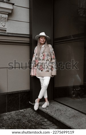 beautiful blonde girl dressed in beige jacket with pink flowers print, white pants, pink loafers, hat, bag, accessories, stylish fashion outfit, full length lifestyle model