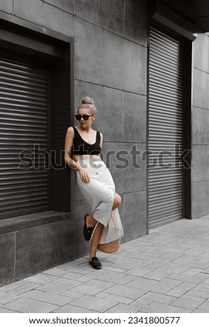 beautiful blonde girl dressed in beige linen skirt, top, mules, straw bag, sunglasses, accessories, bun hairstyle, stylish fashion outfit, full length lifestyle model
