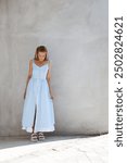 beautiful blonde girl dressed in summer blue and white checkered dress with bows, ruffles and slit, sandals and bag, accessories, stylish fashion outfit, full length lifestyle model