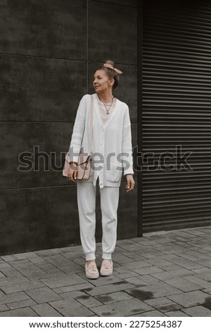 beautiful blonde girl dressed in white knitted suit with pants and cardigan, pink loafers and bag, bun hairstyle, accessories, stylish fashion outfit, full length lifestyle model
