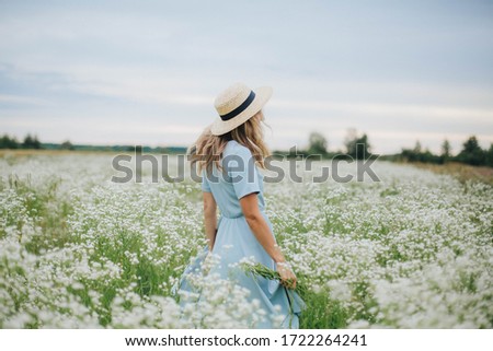 beautiful blonde girl in a field of daisies. woman in a blue dress in a field of white flowers. girl with a bouquet of daisies. summer tender photo in the village. wildflowers. girl in a straw hat