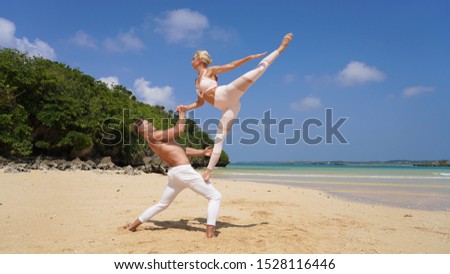 beautiful blonde girl and handsome man in white on the Pacific coast in Asia is engaged in acro yoga, pair acrobatics. duo acrobats circus performers dancers on the beach twine