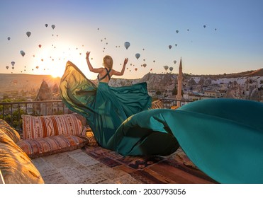 Beautiful blonde girl in the long green dress in Cappadocia romantic morning with sunrise on the amazing background of hundred flying balloons.