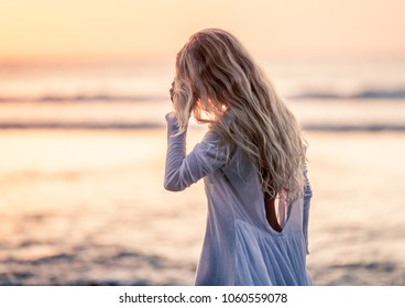 Beautiful blonde girl with long hair in short white dress walking at sunset on the beach in Bali, Indonesia touching hair	
 - Powered by Shutterstock