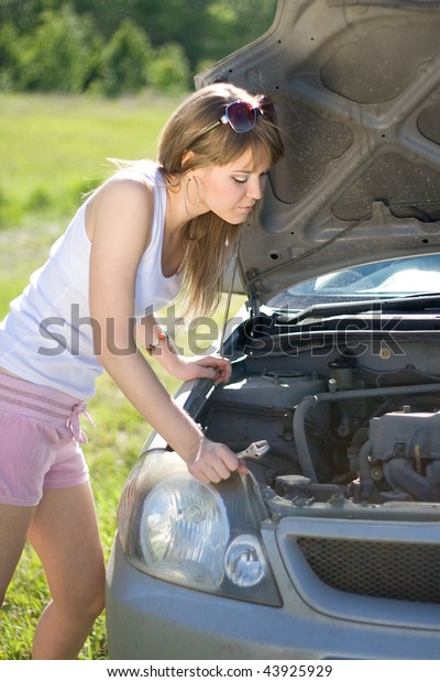 Beautiful\
blonde girl looking under the hood of the\
car
