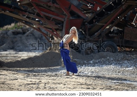 Beautiful blonde girl, model posing with a blue cape, on the background of a metal structure