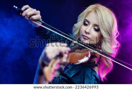 beautiful blonde girl playing violin in neon light on background