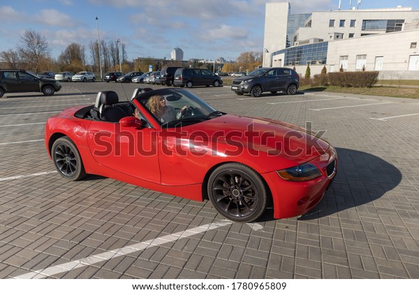 Beautiful blonde girl in a red dress posing in\
a red car in the city on a sunny\
day