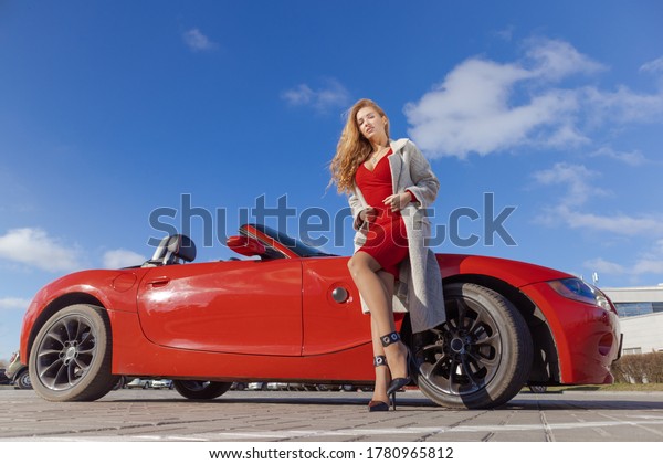 Beautiful blonde girl in a red dress posing in\
a red car in the city on a sunny\
day