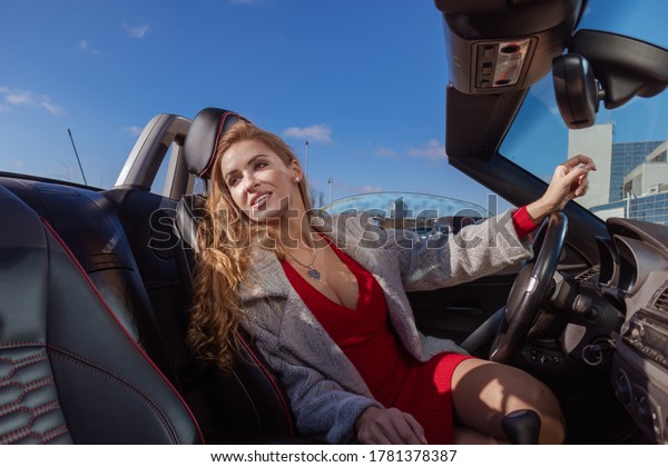 Beautiful blonde girl in a red dress posing in
a red car in the city on a sunny
day