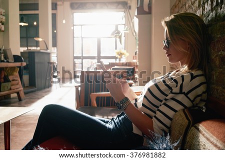Beautiful blonde girl working at a coffee shop with a smart-phone. female freelancer connecting to internet via cellphone. flare light