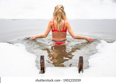 Beautiful blonde hair girl with sexy red swimsuit bathing and swimming in the cold water of a lake or river, cold therapy, ice swim