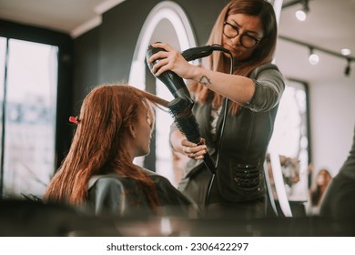 Beautiful blonde hairdresser blowing her clients bangs at the hair salon - Powered by Shutterstock