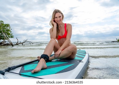 A beautiful blonde model enjoys a summers day while preparing to surf on the ocean with her paddle board
