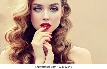 Beautiful  blonde model  girl  with long curly  hair . Hairstyle wavy curls . Red  lips and  nails manicure .  Fashion , beauty and make up portrait