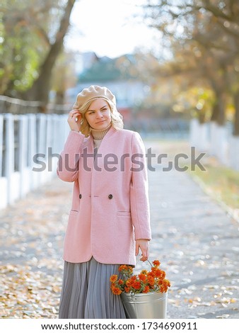 Beautiful blonde model Girl in pink coat posing and looking at the camera. A happy young woman walks and enjoys the Sunny weather. The concept of flowers and happiness