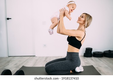 A beautiful blonde mom with a small child in her arms is sitting in the room on a gymnastic rug after fitness classes. Doing sports at home and restoring women's health.
