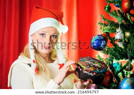 Beautiful blonde in a red cap with chocolate box celebrates Christmas. Christmas photo of blonde in red cap. New Year's holidays and Christmas tree..