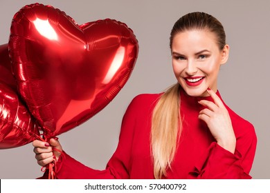Beautiful blonde smiling woman holding red balloons, looking at camera, valentine's day.