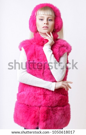 beautiful blonde teen girl dressed in pink fur vest and earmuffs posing in studio over white background