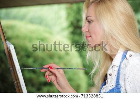 beautiful blonde woman artist with a brush in her hand draws on canvas in the nature.