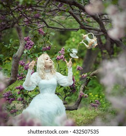 Beautiful Blonde Woman In Blooming Lilac Garden. Vintage. Alice. Fairytale. Surreal Tea Party Concept. 