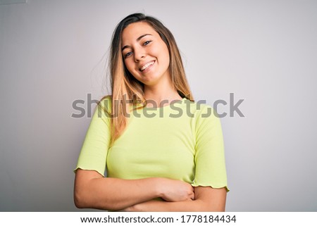 Beautiful blonde woman with blue eyes wearing green casual t-shirt over white background happy face smiling with crossed arms looking at the camera. Positive person.