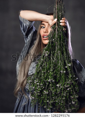Beautiful blonde woman with bouquet of wild flowers smiling on dark wall background