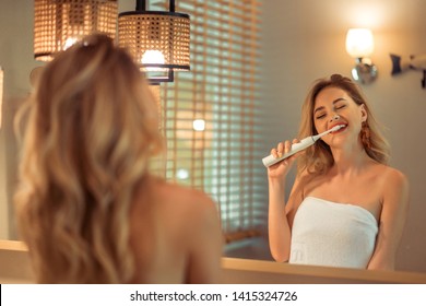 Beautiful blonde woman brushing her teeth using electric toothbrush having fun. Hygiene, body care concept.