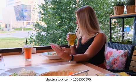 Beautiful Blonde Woman Chatting On The Phone, Talking On Skype And Drinking A Cocktail, Sitting In A Cafe On The Street