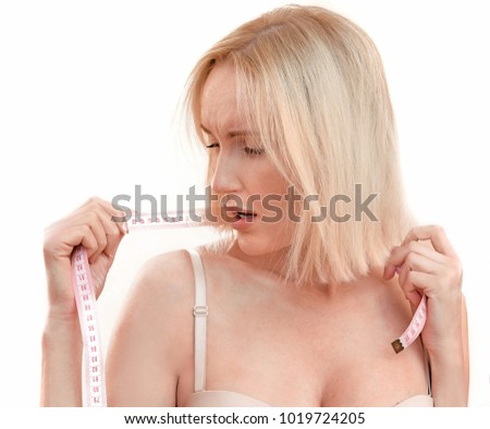 Beautiful blonde woman with clean healthy skin and big breasts is measuring herself with a measuring tape and having problems with it She is concerned about her size, maybe she gained weight of fat.