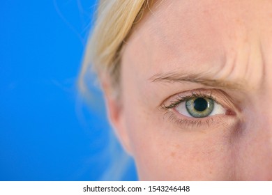 Beautiful Blonde Woman With Clean Skin And Frekles Frown Her Brows Over Bright Blue Background. Thin Brows And Blue Eyes. Thundery Brow And Sad Look