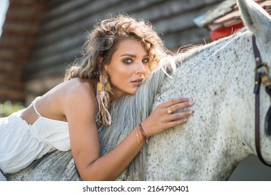 Beautiful blonde woman with curly hair and horse. Portrait of a girl with white dress and her horse. Beautiful girl interacting and having fun with a horse at the ranch