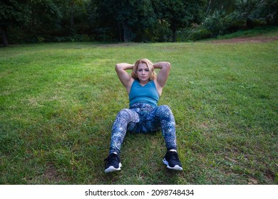 beautiful blonde woman doing calisthenics and abdominal exercises in the park on the grass. The woman is fat and needs to do sport and eat a healthy diet. Calisthenics concept and healthy diet.