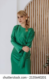 A beautiful blonde woman in an elegant green silk dress poses in a bright room. Holiday preparation, beauty industry. Soft selective focus.