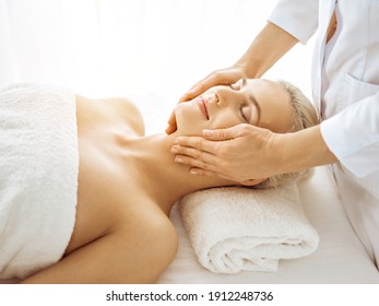 Beautiful Blonde Woman Enjoying Facial Massage With Closed Eyes In Sunny Spa Center. Relaxing Treatment In Medicine And Beauty Concepts