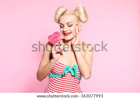Beautiful blonde woman with glamour bright makeup holding pink lollipop heart. Valentines day concept.