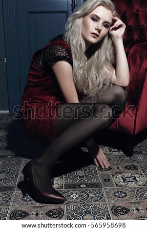 Beautiful blonde woman with hair and make-up sitting on the floor near the red chair