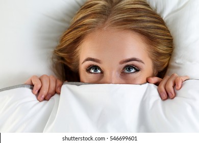 Beautiful Blonde Woman Hiding Face Under Cover Lying In Bed. Female Sparky Eyes Looking Up Closeup. Sweet Dreams, Flirtation, Playing Game, Wake Up In Strange Place, Shame, Casual Sex Concept